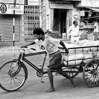 A worker handling his loaded tricycle in an ascending road. Madurai, Tamil Nadu, India.